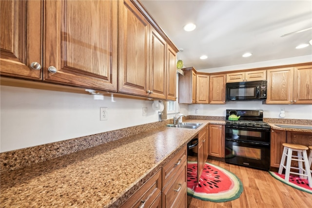 kitchen with light stone countertops, black appliances, light hardwood / wood-style flooring, and sink