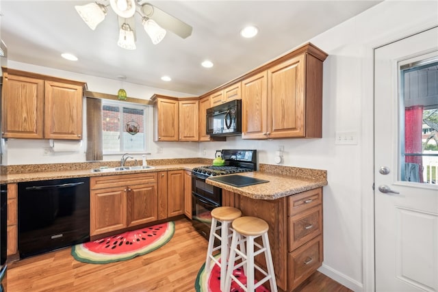 kitchen with black appliances, ceiling fan, sink, light hardwood / wood-style floors, and a kitchen bar