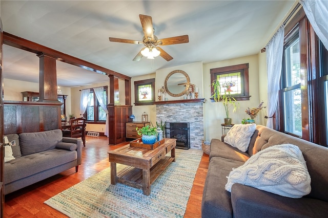 living room featuring ceiling fan, a stone fireplace, decorative columns, and hardwood / wood-style floors