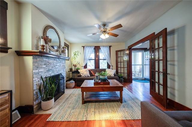 living room with french doors, wood-type flooring, ceiling fan, and a stone fireplace