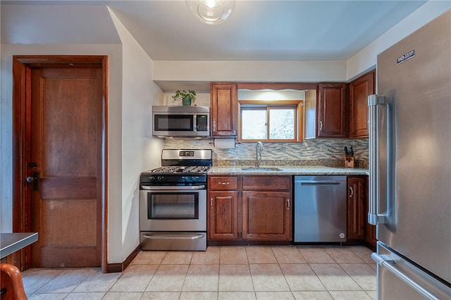 kitchen featuring sink, light stone countertops, backsplash, appliances with stainless steel finishes, and light tile patterned floors