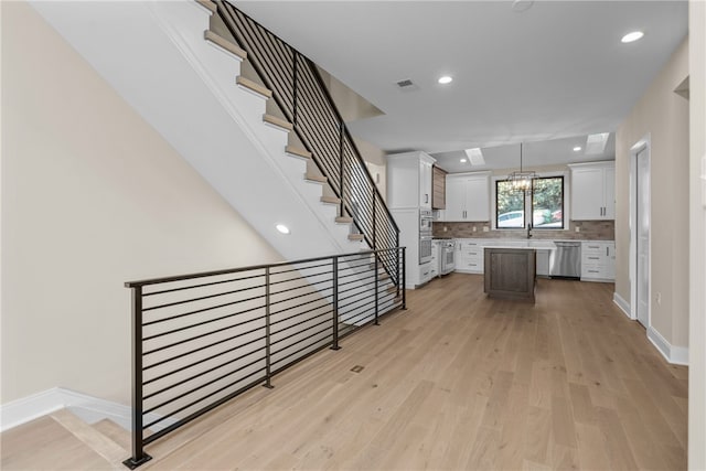 kitchen featuring a center island, light hardwood / wood-style floors, white cabinetry, decorative light fixtures, and dishwasher