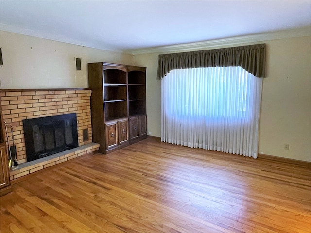 unfurnished living room with ornamental molding, a brick fireplace, and light hardwood / wood-style floors