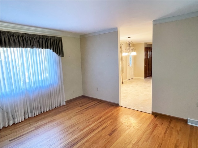 empty room featuring ornamental molding, light wood-type flooring, and a chandelier