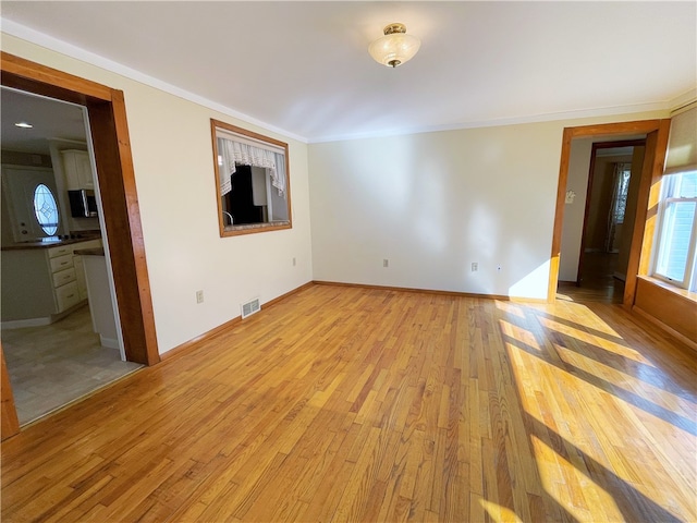 empty room with ornamental molding and light hardwood / wood-style floors