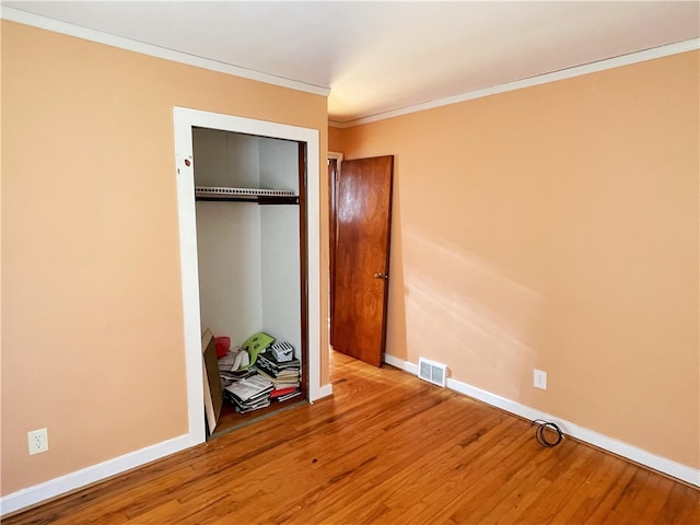 unfurnished bedroom featuring wood-type flooring, a closet, and ornamental molding