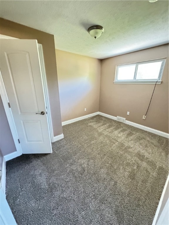 unfurnished bedroom with dark colored carpet and a textured ceiling