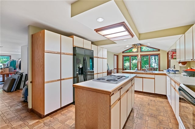 kitchen with white cabinets, lofted ceiling, kitchen peninsula, a kitchen island, and appliances with stainless steel finishes