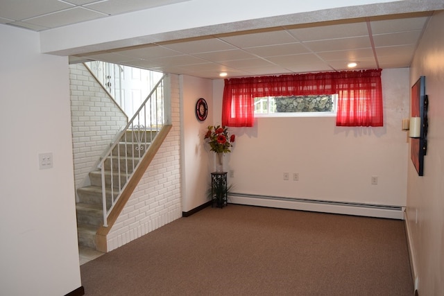 basement featuring a paneled ceiling, brick wall, carpet flooring, and a baseboard radiator