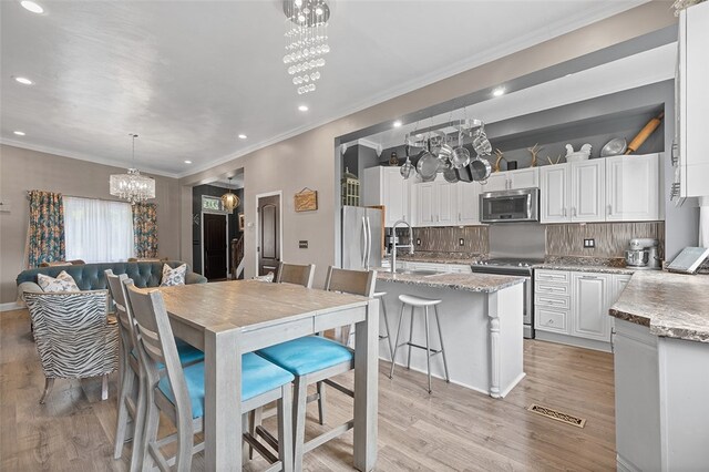 kitchen with light hardwood / wood-style floors, white cabinets, hanging light fixtures, a kitchen island with sink, and appliances with stainless steel finishes