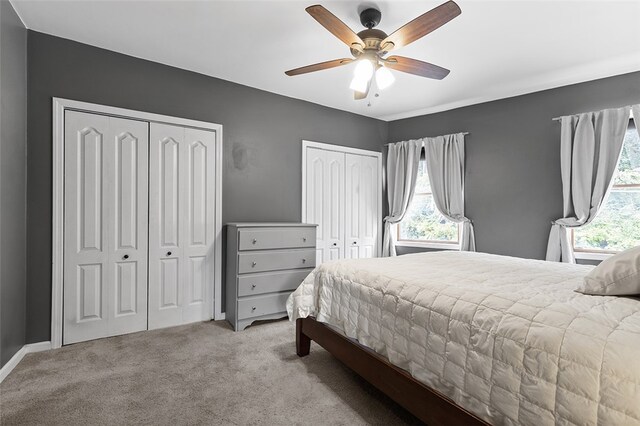 bedroom with multiple closets, light colored carpet, and ceiling fan