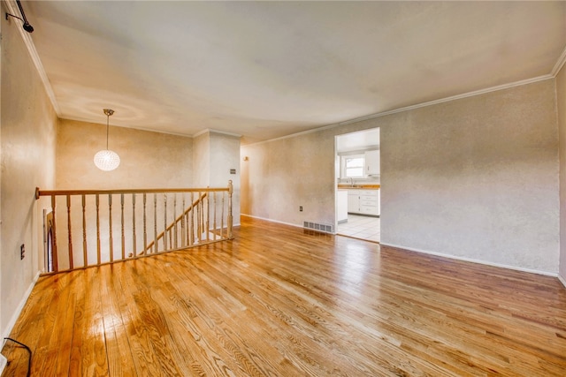 unfurnished room featuring an inviting chandelier, light wood-type flooring, crown molding, and sink