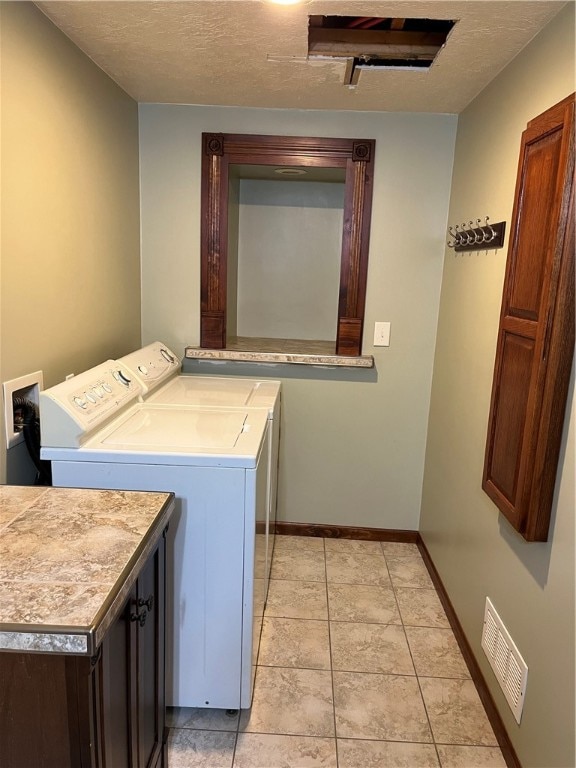 washroom featuring washing machine and dryer, cabinets, light tile patterned floors, and a textured ceiling