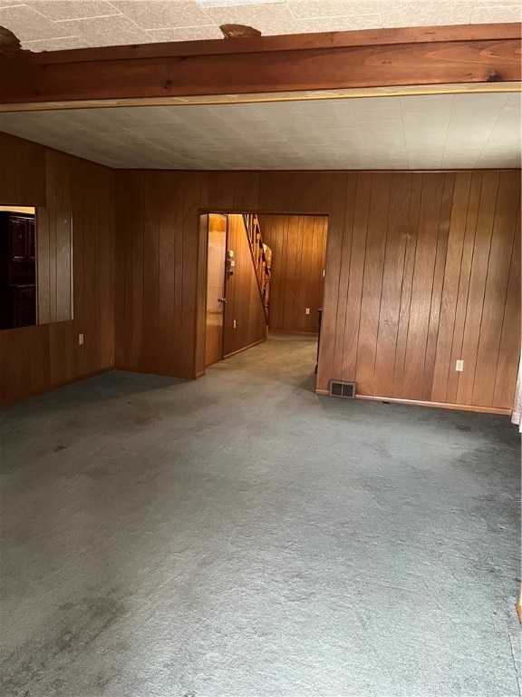 empty room featuring wooden walls, beam ceiling, and carpet floors