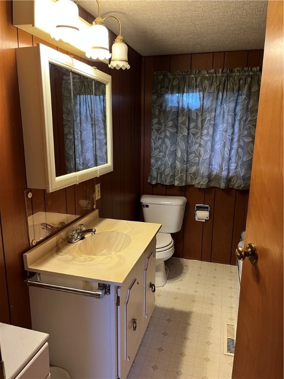 bathroom with a textured ceiling, wooden walls, vanity, and toilet