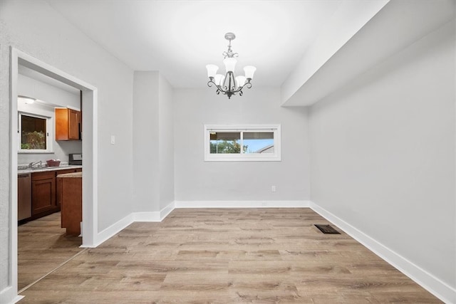 unfurnished dining area featuring light wood-type flooring, sink, and an inviting chandelier