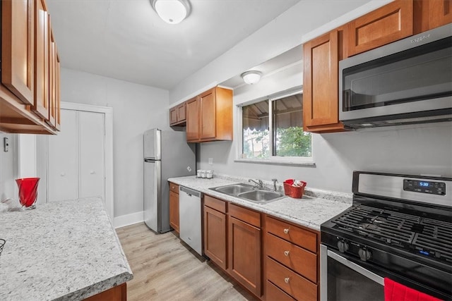 kitchen with stainless steel appliances, light stone countertops, light hardwood / wood-style floors, and sink