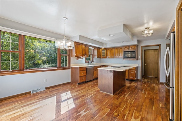 kitchen with pendant lighting, a kitchen island, stainless steel appliances, a notable chandelier, and dark hardwood / wood-style flooring