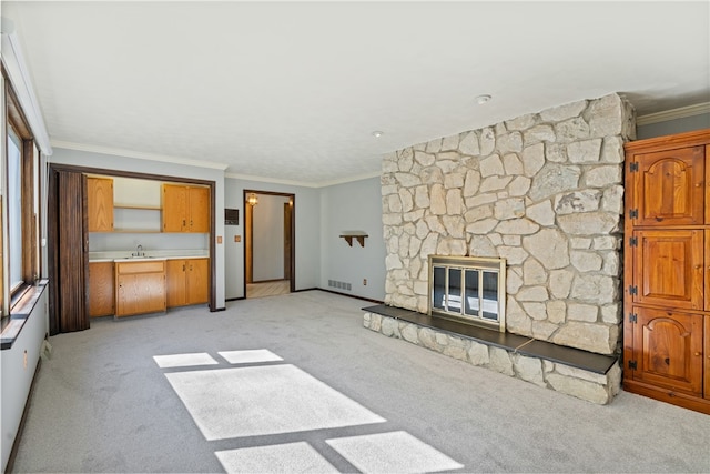 unfurnished living room featuring a stone fireplace, light colored carpet, crown molding, and sink