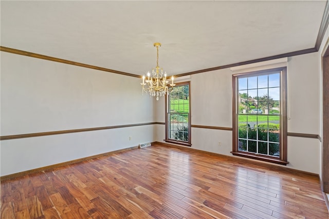 empty room featuring wood-type flooring, a notable chandelier, and ornamental molding