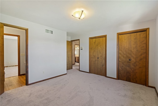 unfurnished bedroom featuring light colored carpet and two closets