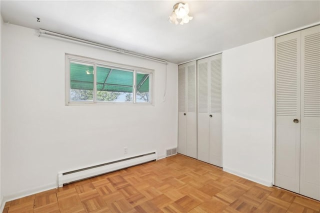 unfurnished bedroom featuring two closets, light parquet flooring, and baseboard heating