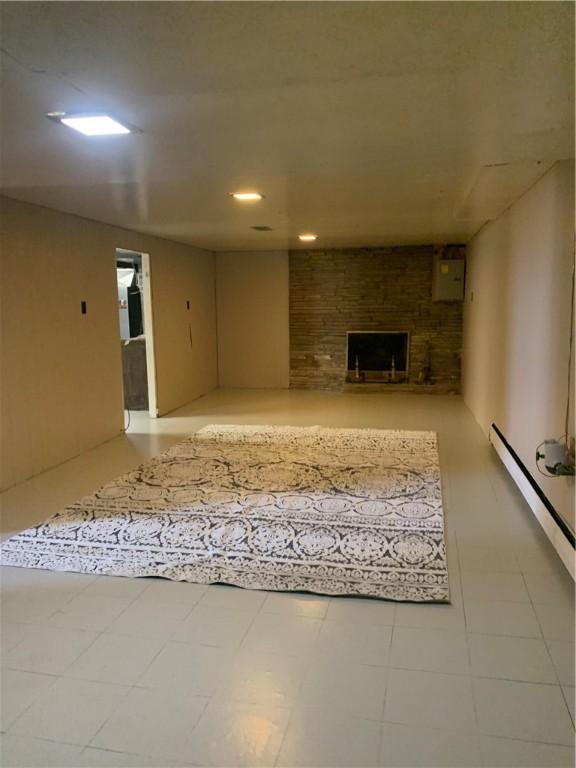 basement featuring a brick fireplace, a baseboard heating unit, and light tile patterned floors