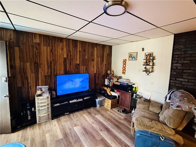 living room with a paneled ceiling, wood walls, and light hardwood / wood-style floors