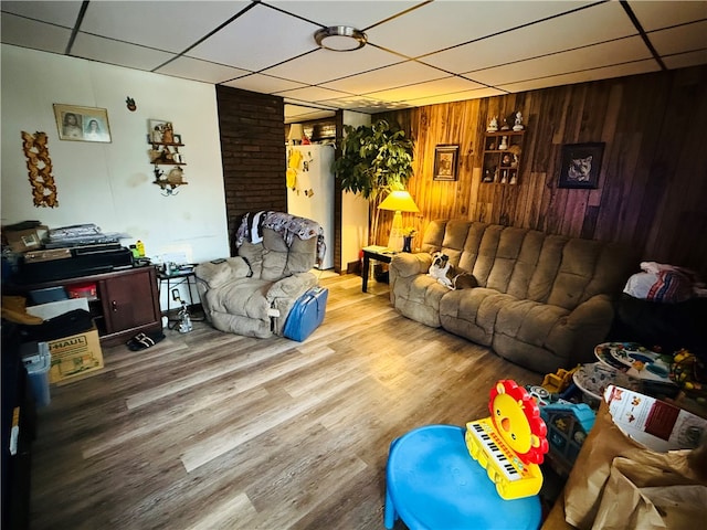 living room featuring wood-type flooring, a drop ceiling, and wooden walls