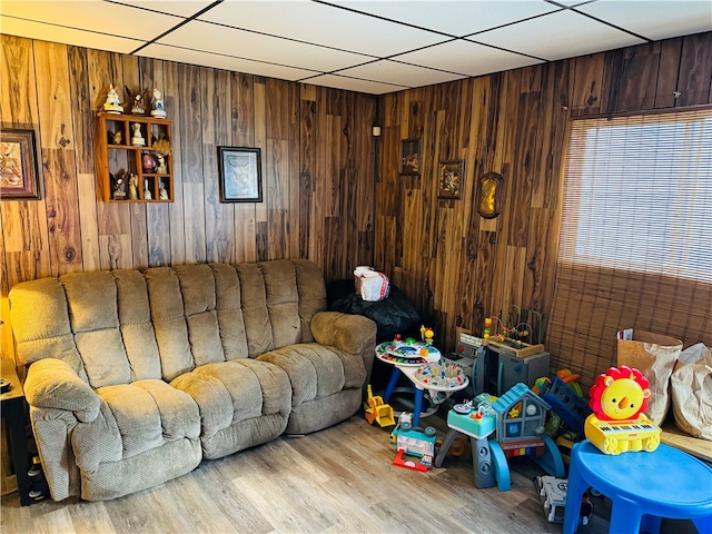 living room with a paneled ceiling, wooden walls, and light hardwood / wood-style flooring