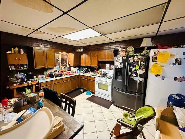 kitchen with a paneled ceiling, light tile patterned flooring, white appliances, and brick wall