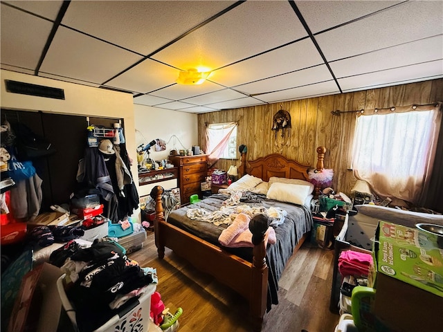 bedroom featuring a paneled ceiling, dark hardwood / wood-style floors, and wood walls