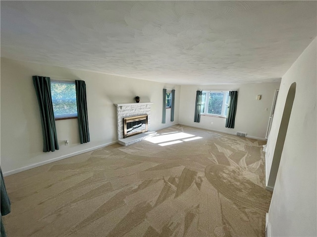 unfurnished living room with light colored carpet, a textured ceiling, a fireplace, and a healthy amount of sunlight