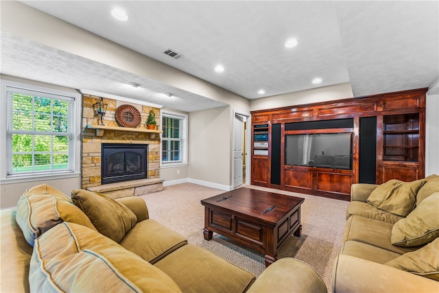 living room with a stone fireplace, carpet, and a healthy amount of sunlight