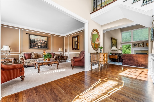 living room with a fireplace, wood-type flooring, crown molding, and a towering ceiling