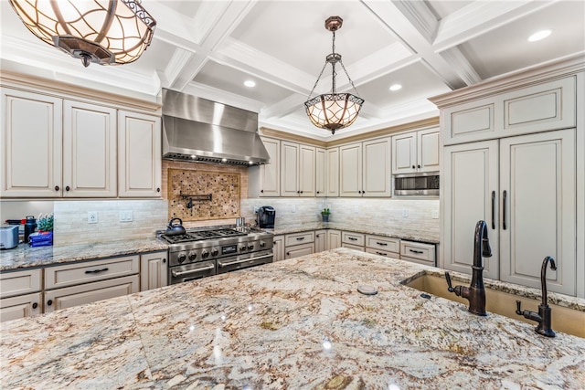 kitchen featuring decorative light fixtures, wall chimney exhaust hood, coffered ceiling, stainless steel appliances, and light stone countertops