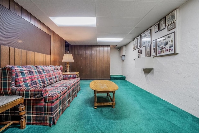 carpeted living room with wood walls and a drop ceiling