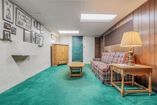 living area with wooden walls, a paneled ceiling, and carpet flooring