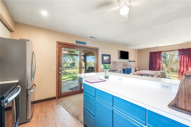 kitchen with ceiling fan, stainless steel electric stove, blue cabinetry, light hardwood / wood-style floors, and a fireplace