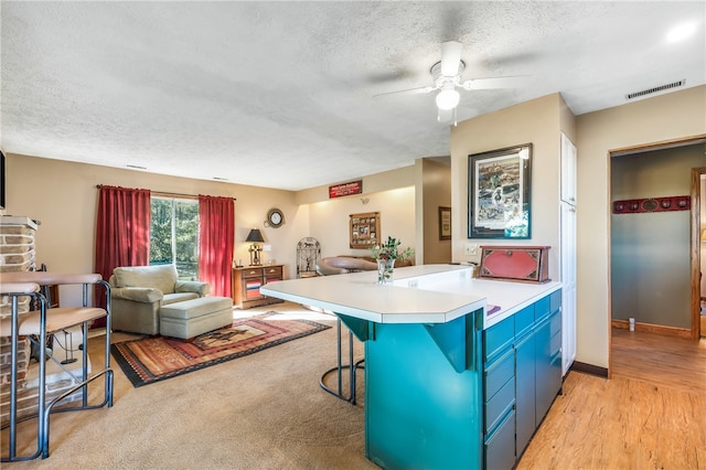 kitchen with ceiling fan, light hardwood / wood-style flooring, kitchen peninsula, a kitchen bar, and a textured ceiling