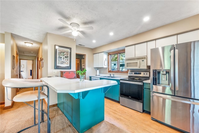 kitchen with light wood-type flooring, a kitchen island, stainless steel appliances, white cabinets, and a textured ceiling