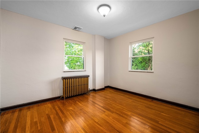 spare room featuring wood-type flooring, radiator heating unit, and a healthy amount of sunlight