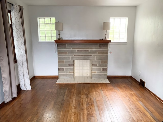 unfurnished living room with dark wood-type flooring, a fireplace, and a healthy amount of sunlight