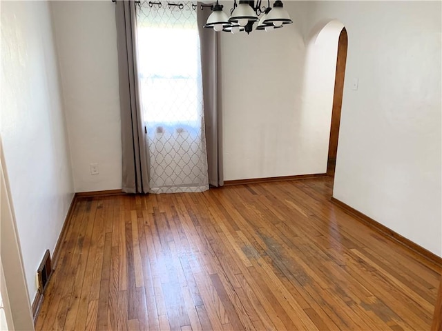 spare room with a chandelier, visible vents, baseboards, arched walkways, and hardwood / wood-style flooring