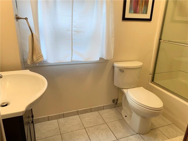 full bathroom featuring toilet, bath / shower combo with glass door, tile patterned floors, and baseboards