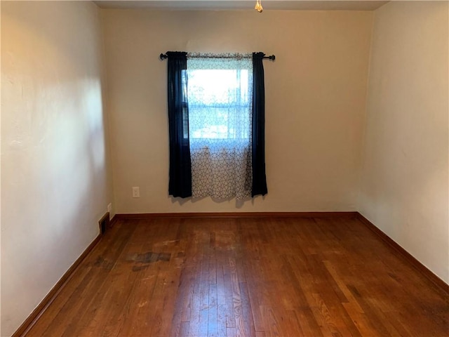 empty room with visible vents, hardwood / wood-style flooring, and baseboards