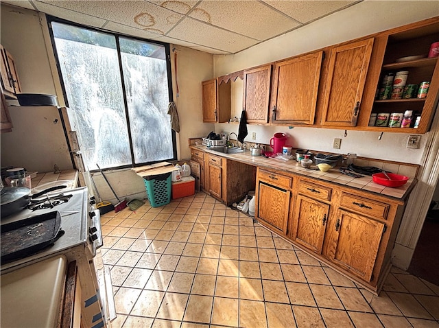 kitchen featuring light tile patterned floors, a paneled ceiling, sink, white gas stove, and tile countertops