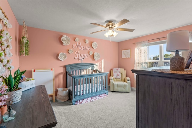 bedroom with ceiling fan, carpet flooring, a textured ceiling, and a crib