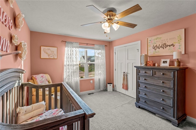 bedroom featuring a textured ceiling, a closet, ceiling fan, light carpet, and a nursery area