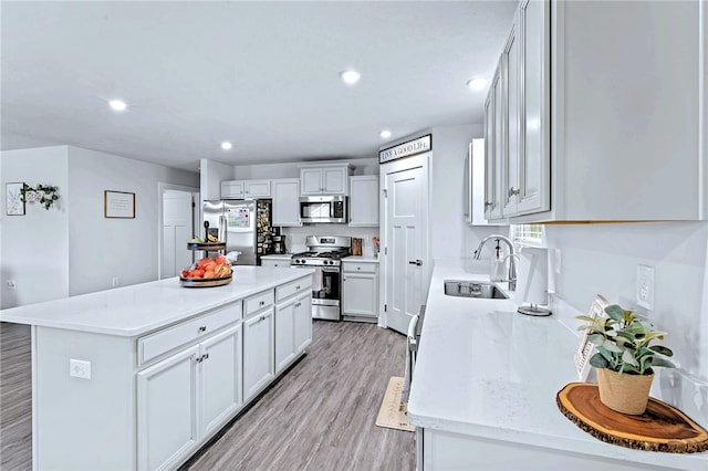 kitchen with appliances with stainless steel finishes, light wood-style floors, white cabinets, a sink, and a kitchen island